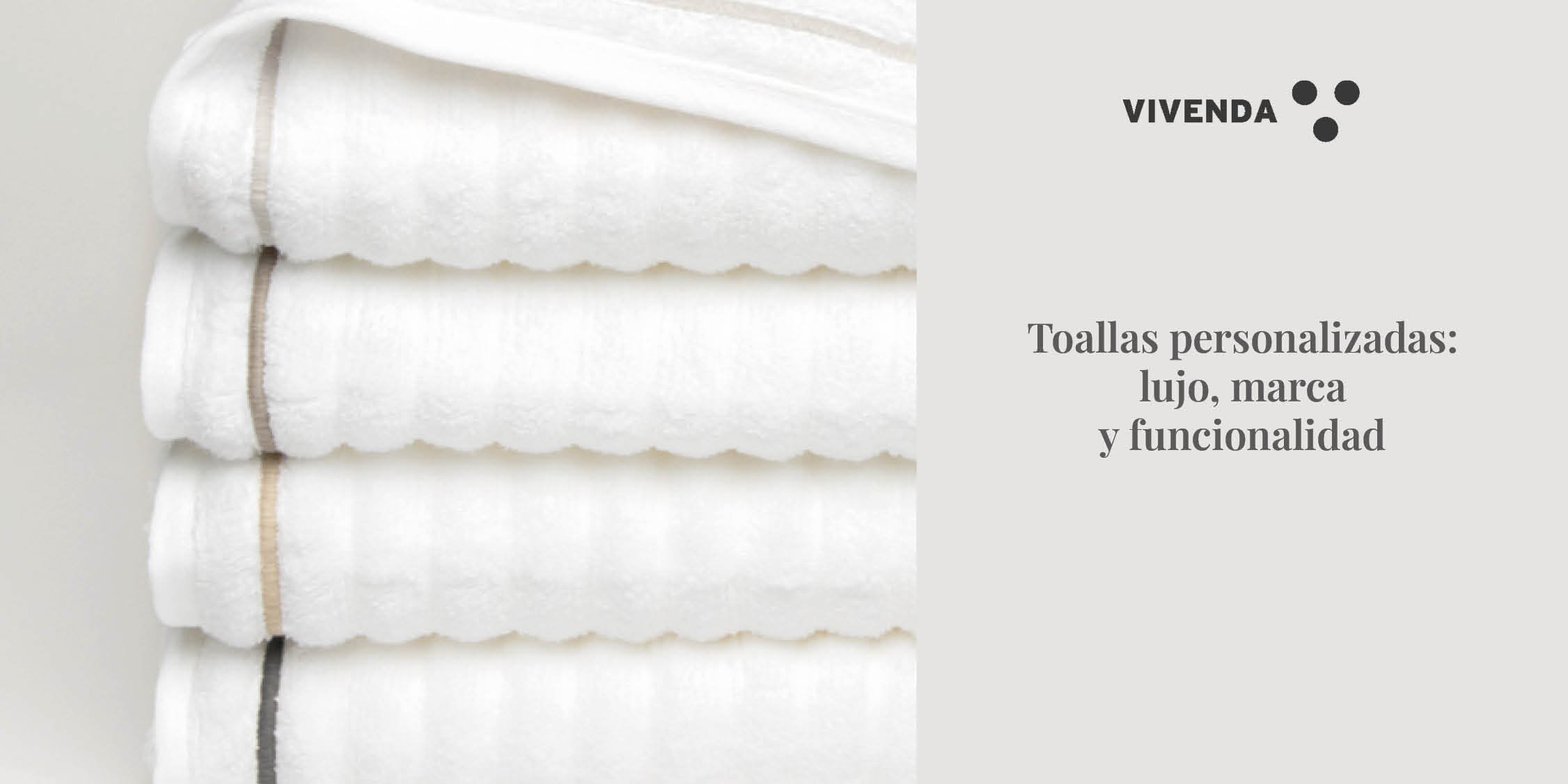 Set de toallas blancas Vivenda personalizadas con iniciales bordadas en festón. Están dobladas sobre una charola de baño estilo boutique con detalles de madera clara y elementos naturales. Representa exclusividad, cuidado al detalle y lujo accesible.