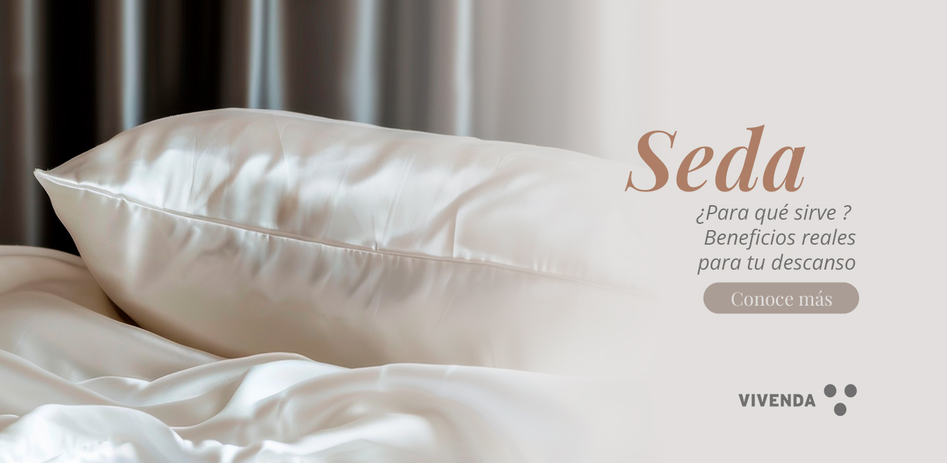 Primer plano de una almohada de seda color marfil sobre cama neutra, con luz suave y textura brillante.